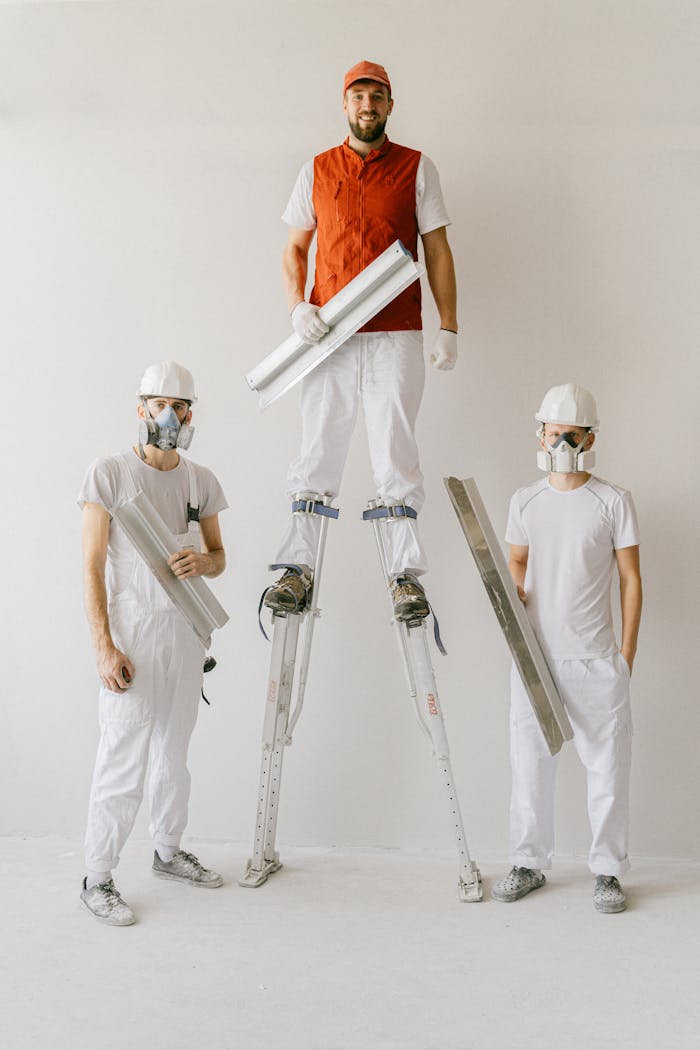 Construction workers in uniforms and hard hats using drywall stilts indoors.