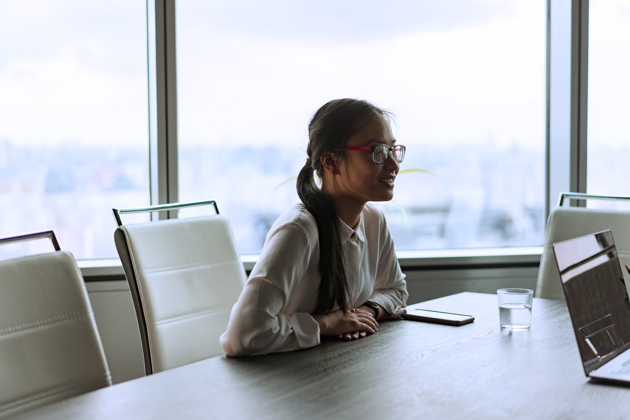 Smiling Asian woman in business meeting with laptop and notepad.